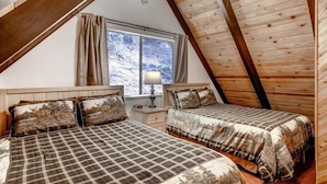 A cozy attic bedroom with two beds, wooden beams, a window with a view of a snowy landscape, and a lamp on a bedside table.