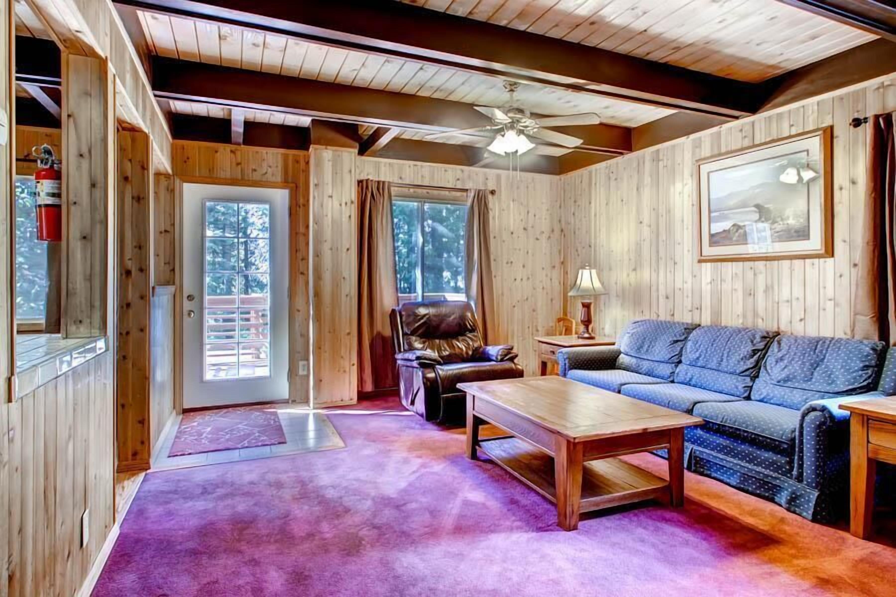Un interior de cabaña acogedor, con detalles de madera, un ventilador de techo, un sofá, una butaca y una mesa de centro.