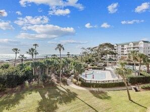 A resort with a swimming pool, palm trees, and a view of the ocean.