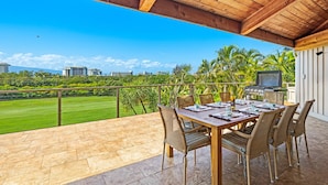 A covered outdoor dining area with a view of a golf course and palm trees.