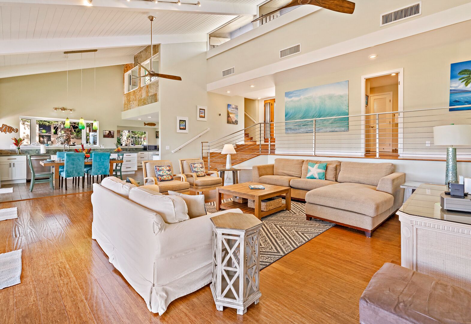A spacious living area with a high ceiling, a staircase, and a kitchen in the background.