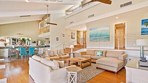 A spacious living area with a high ceiling, a staircase, and a kitchen in the background.
