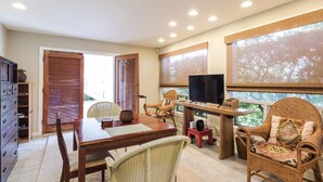 A room with a wooden dining table, wicker chairs, a television, and large windows with blinds. - Loft In Kailua - Spacious with Parking, Internet and minutes to Kailua Beach! (Kailua)