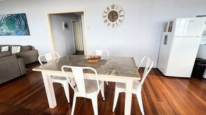 A dining area with a wooden table, white chairs, and a wall clock.
