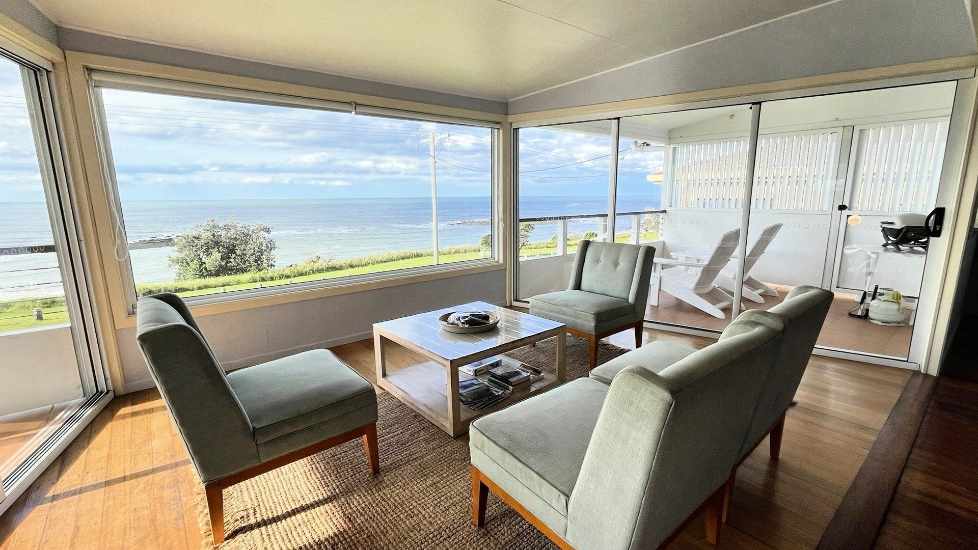 Un salon moderne avec vue sur la mer, comprenant un canapé, deux fauteuils et une table basse.