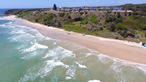 Una playa costera con olas, una orilla arenosa y edificios al fondo.