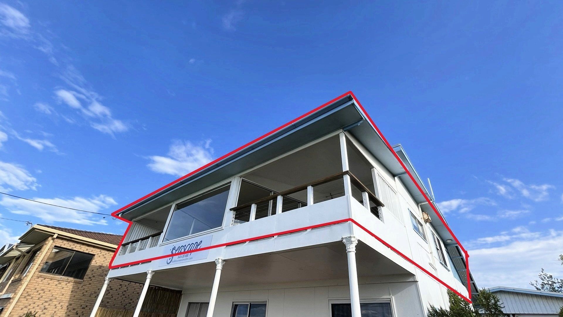 A two-story building with a balcony on the upper floor, a visible sign with a phone number, and a clear blue sky in the background.