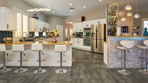 Een moderne keuken met een centraal eiland, een paar barkrukken, roestvrijstalen apparatuur en een spatwand met een geometrisch patroon.