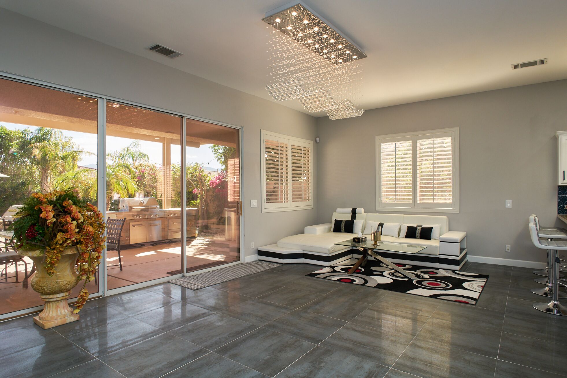 A spacious living room with a large sliding glass door leading to an outdoor patio, a modern chandelier, and a sectional sofa with decorative pillows.