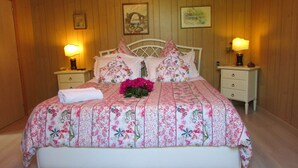 A bedroom with a wooden paneled wall, a bed with floral bedding, two bedside tables with lamps, and framed pictures on the wall. - B&B Palazzo a Mare (Capri)