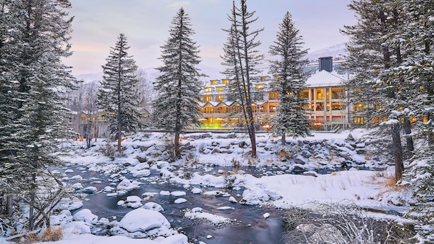 A lodge with a river in the foreground, surrounded by snow-covered trees. - Inviting, cabin like condo, close to Gore Creek w/ access to all Grand Hyatt Amenities (Vail)