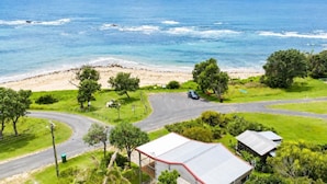 Um imóvel à beira-mar com entrada pavimentada, um carro estacionado na rua e uma praia ao fundo.