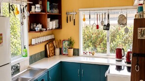 A kitchen with teal cabinets, a window with hanging utensils, and a red kettle on the counter.