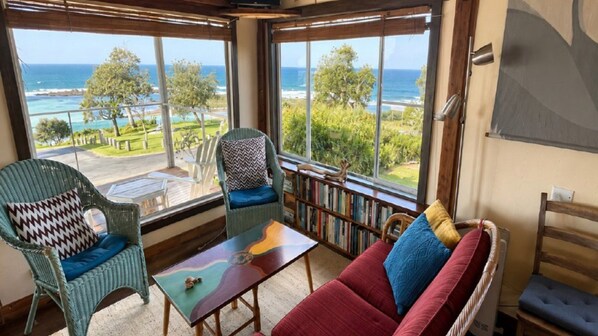 A cozy room with a view of the ocean, featuring wicker furniture, a red sofa, and a wooden coffee table.