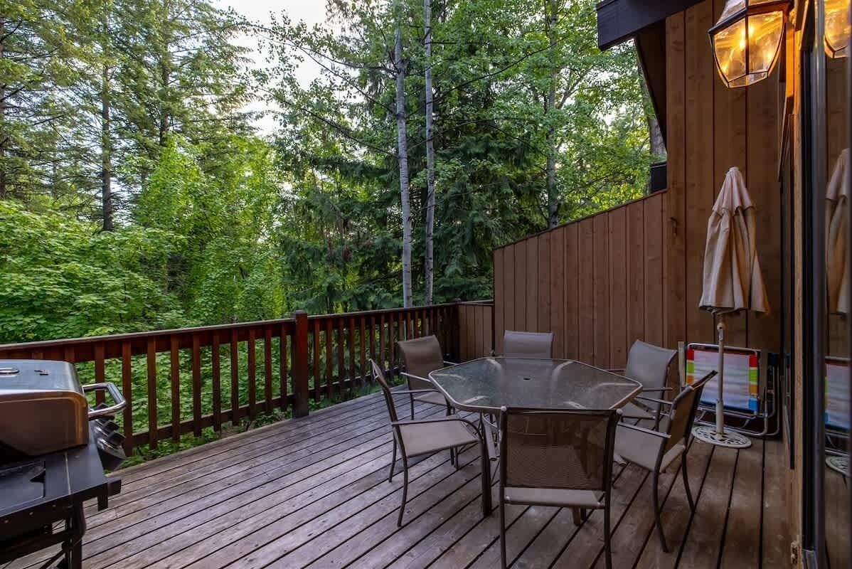 A wooden deck with a table and chairs, a grill, and a wooden wall with a lantern.