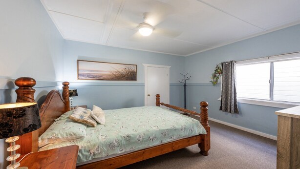 A bedroom with a single bed, a bedside table, a lamp, a ceiling fan, a window with curtains, and a door. - Wooli House - Cosy cottage overlooking the river (Wooli)