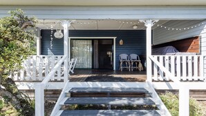 A wooden deck with a white railing, a set of steps leading to a door, and a small table with chairs outside a building. - Wooli House - Cosy cottage overlooking the river (Wooli)