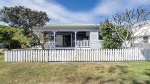 A single-story house with a porch, a picket fence, and a lawn. - Wooli House - Cosy cottage overlooking the river (Wooli)