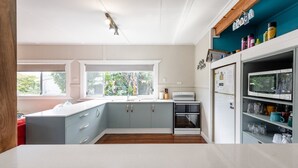A modern kitchen with grey cabinets, a white countertop, a built-in oven, and a refrigerator with magnets and notes. - Wooli House - Cosy cottage overlooking the river (Wooli)