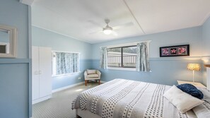 A bedroom with a bed, a chair, a window, and a ceiling fan.