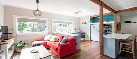 Un soggiorno moderno con un divano rosso, pavimento in legno, angolo cottura con una parete decorata in blu e zona pranzo con sedie in legno.