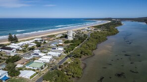 An aerial view of a coastal residential area with houses, a road, and a beach.
