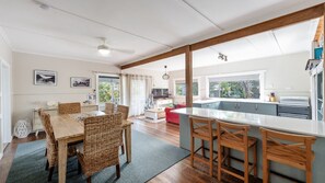 Eine geräumige Küche mit einer großen Kochinsel, einem Holzespeisetisch mit Korbstühlen und einem gemütlichen Wohnbereich mit einem roten Sofa.