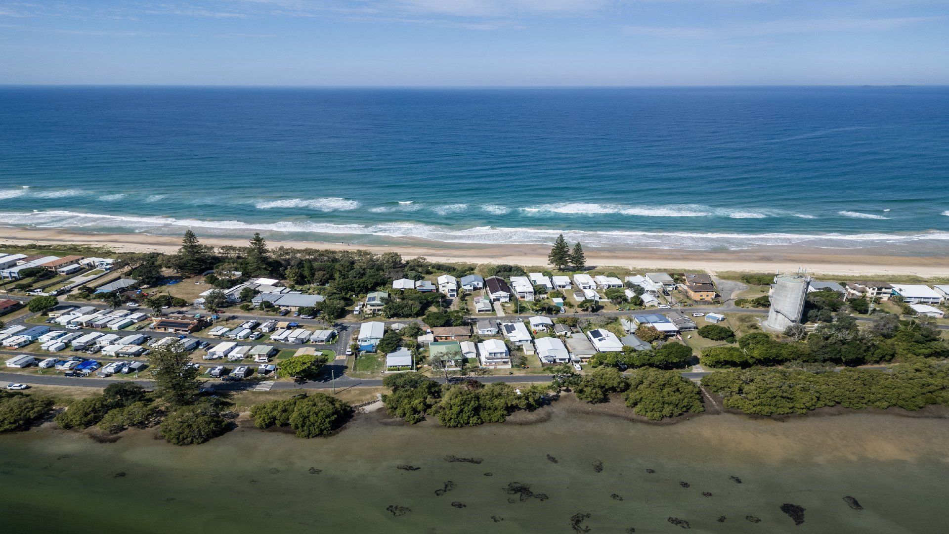An aerial view of a coastal residential area with houses, a beach, and a marina.