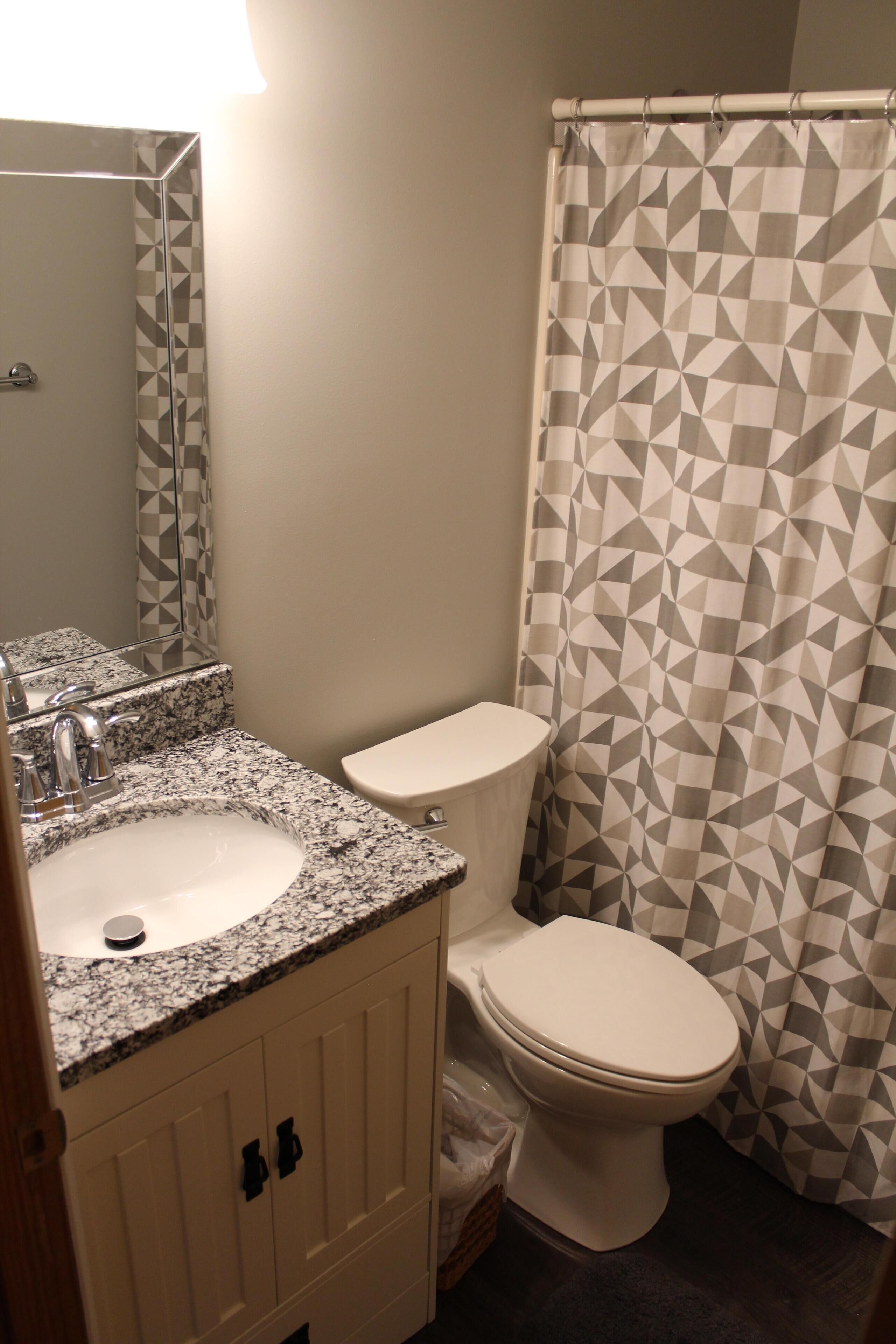 Un baño con lavamanos de encimera de granito, inodoro y cortina de ducha con diseño geométrico.