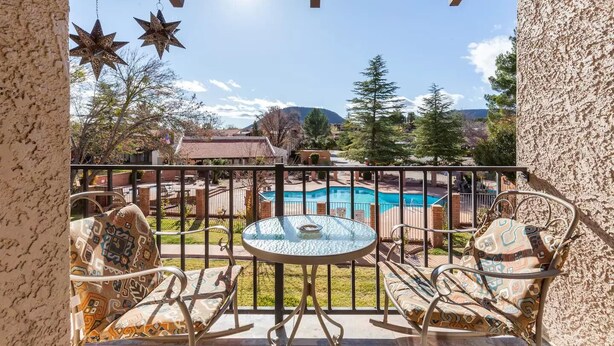 A balcony with a glass table and chairs, a pool, and a mountainous backdrop.