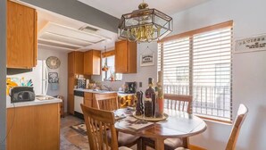 A kitchen with wooden cabinets, a dining table with chairs, a chandelier, and a window with blinds.