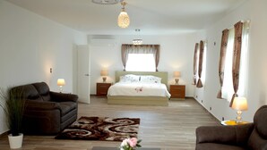 A modern bedroom with a large bed, two bedside tables with lamps, a sofa, a coffee table with decorative items, and a patterned rug. - Pueblo Checo - Czech Guest-House (Cabarete)