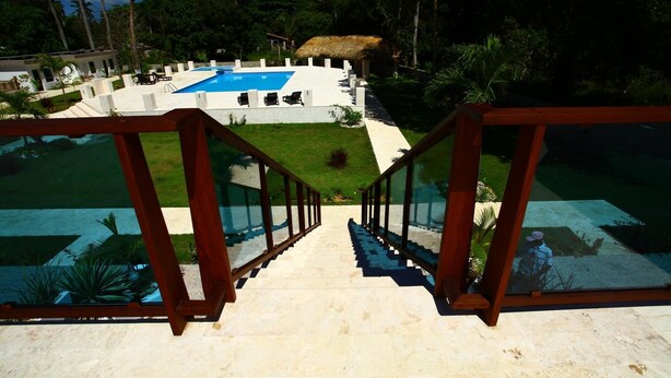 A staircase leading to a pool area with a thatched-roof structure in the background. - Pueblo Checo - Czech Guest-House (Cabarete)