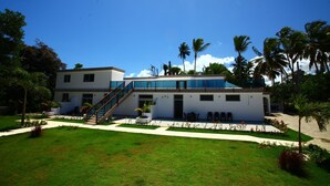 A modern two-story building with a covered outdoor area, surrounded by lush greenery and palm trees. - Pueblo Checo - Czech Guest-House (Cabarete)
