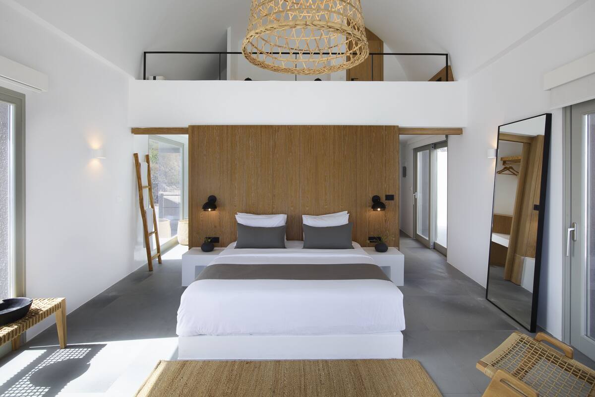 A modern bedroom with a large bed, a wooden headboard, a woven light fixture, and a large mirror.