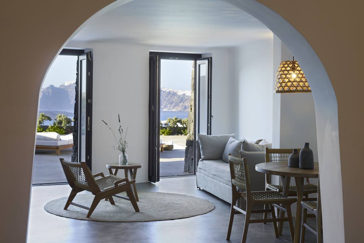 A modern living room with a view of mountains, a sofa, a dining table, and a chair.