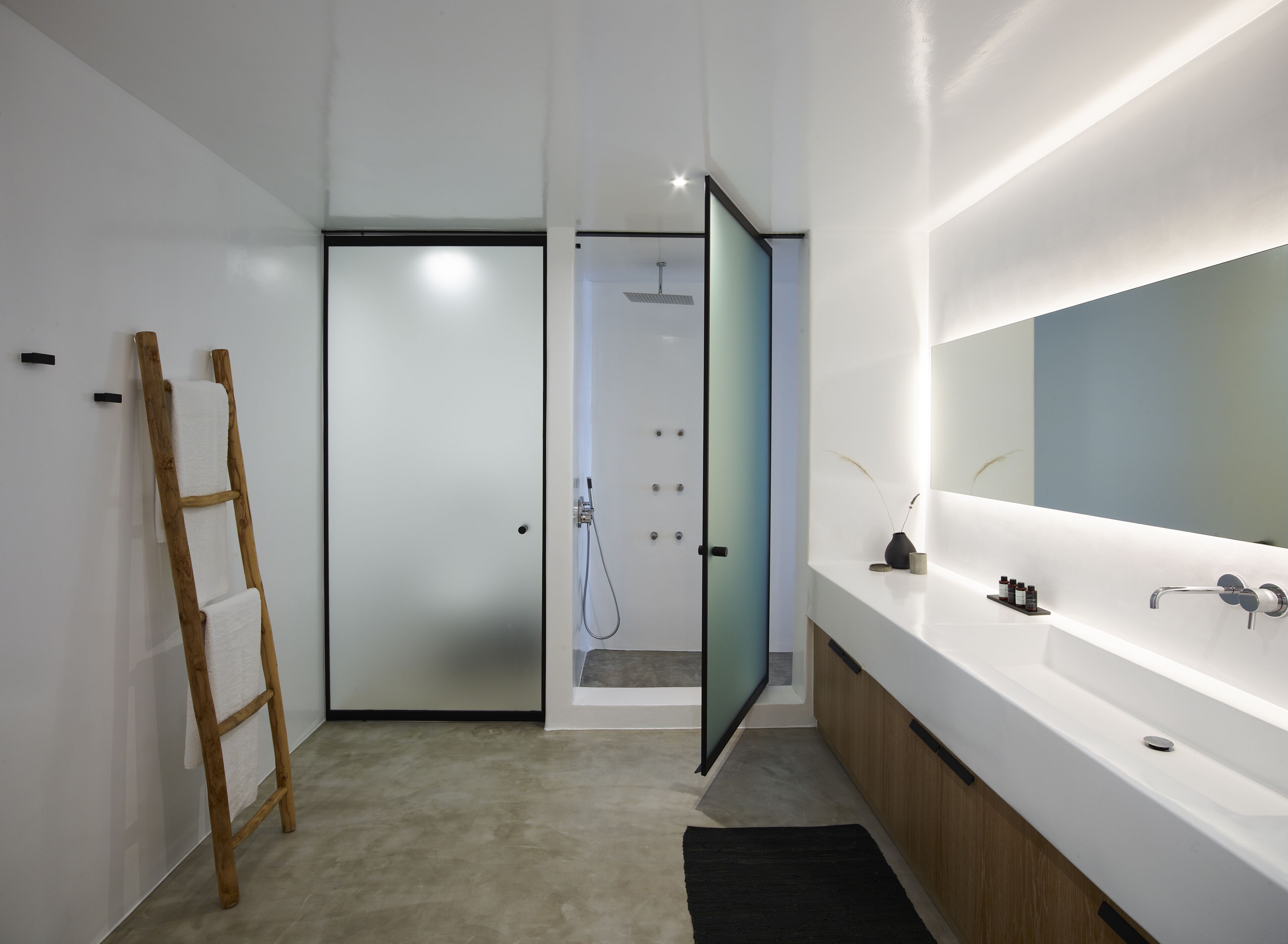 A modern bathroom with a large mirror, a wooden ladder, and a shower area.