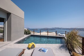 A modern outdoor pool area with a clear view of the sea and distant hills. - Melidonia Suites (Santorini)