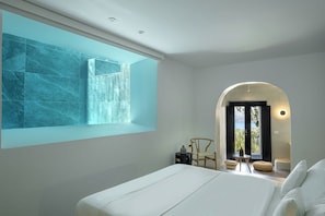 A modern bedroom with a large bed, a view of the outdoors through a window, and a unique ceiling design. - Melidonia Suites (Santorini)