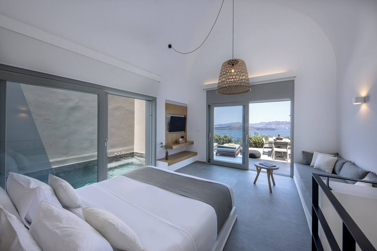 A modern bedroom with a large bed, a TV, a balcony with a view, and a dining area.
