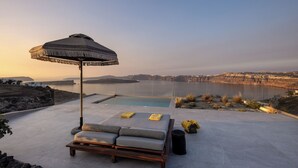 A poolside lounge with a view of the sea and distant hills. - Melidonia Suites (Santorini)