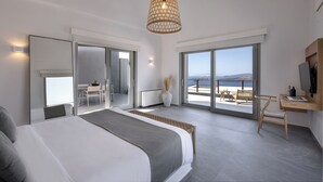 A modern bedroom with a large bed, a balcony with a view, and a dining area. - Melidonia Suites (Santorini)