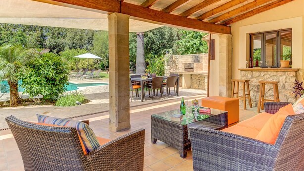 Une terrasse extérieure avec des meubles en osier, un barbecue en pierre et une piscine.
