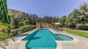 Une piscine rectangulaire bordée de pierres, entourée d’un jardin bien entretenu et d’un mur de pierres.