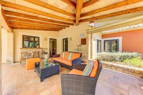 A covered patio area with wicker furniture, stone walls, and a view of the garden. - Llenyater for families with pool (Pollensa)