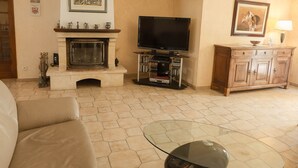 A living room with a fireplace, a television, a cabinet, and a glass coffee table. - Lovely house near the historical center of Narbonne and main shops, private pool (Narbonne)