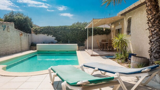 A swimming pool with two lounge chairs, a covered patio area, and a stone wall. - Lovely house near the historical center of Narbonne and main shops, private pool (Narbonne)