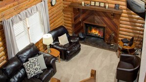 Interior d'una cabana de fusta amb una llar de foc, un sofà de pell i un ventilador de sostre.