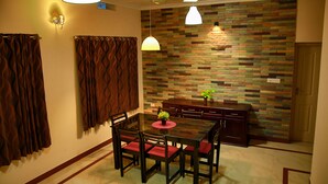 A dining area with a wooden table, red cushioned chairs, a small potted plant, and a stone-patterned wall. - Dvārakā: Luxury Villas of Guruvayur (Guruvayur)
