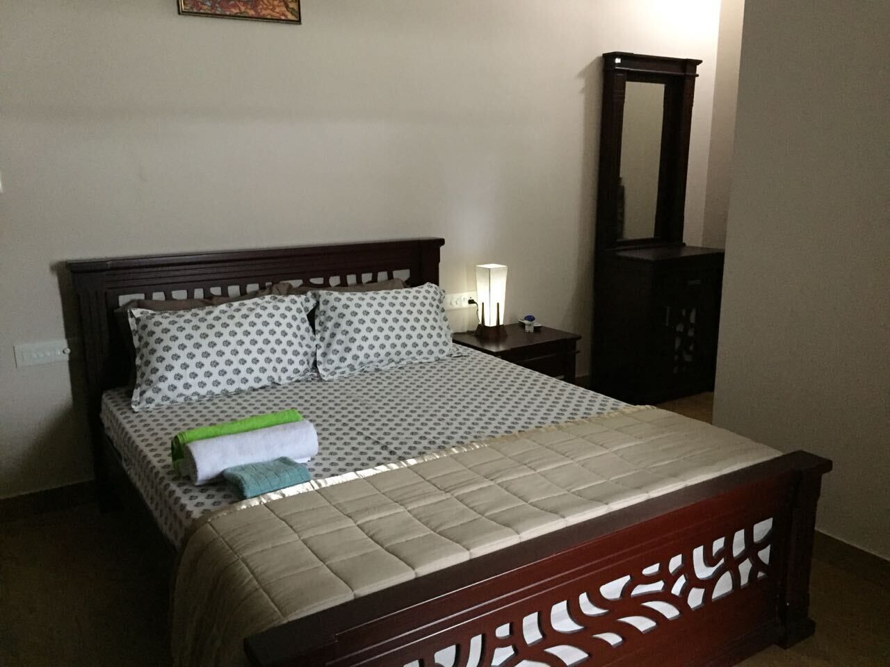 Un lit bien fait, avec une couvre-lit à motifs, une serviette verte et blanche, et une tête de lit en bois.